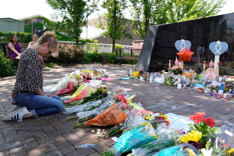 A woman mourns in front of a memorial with bouquets