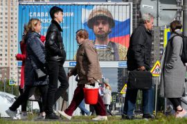 People in St Petersburg walk past a billboard with a portrait of a Russian soldier awarded for action in Ukraine