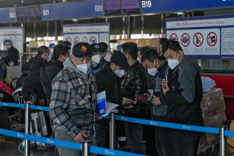 Masked travellers check their passports as they line up at the international flight check in counter at the Beijing Capital International Airport in Beijing, Thursday
