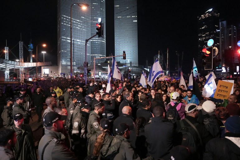 Israeli border police officers prevent protesters from blocking a highway during a rally against the government's plans to overhaul the country's legal system, in Tel Aviv, Israel, Saturday, Jan. 14, 2023. Tens of thousands of Israelis have gathered in central Tel Aviv to protest plans by Prime Minister Benjamin Netanyahu's new government to overhaul the country's legal system and weaken the Supreme Court. 