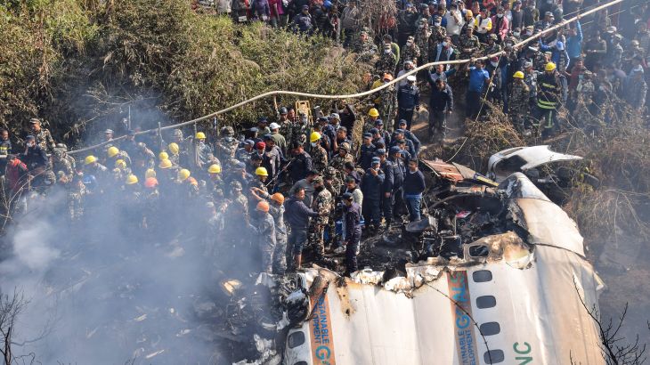 Nepalese rescue workers and civilians gather around the wreckage of a passenger plane that crashed in Pokhara, Nepal