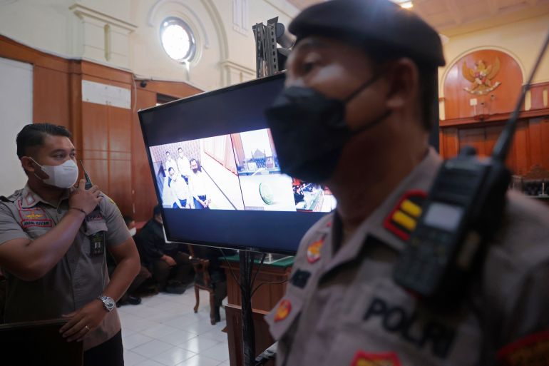 Police officers in court next to a video screen as the trial of five police officers and match officials begins in Surabaya, Indonesia.