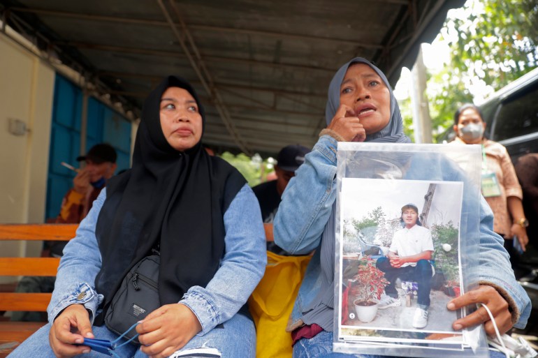 Rini Hanifah sitting on a wooden bench outside the Surabaya court holding a picture of her son Agus Riyansah who died in the October stampede. Rini is with a friend and she is crying.