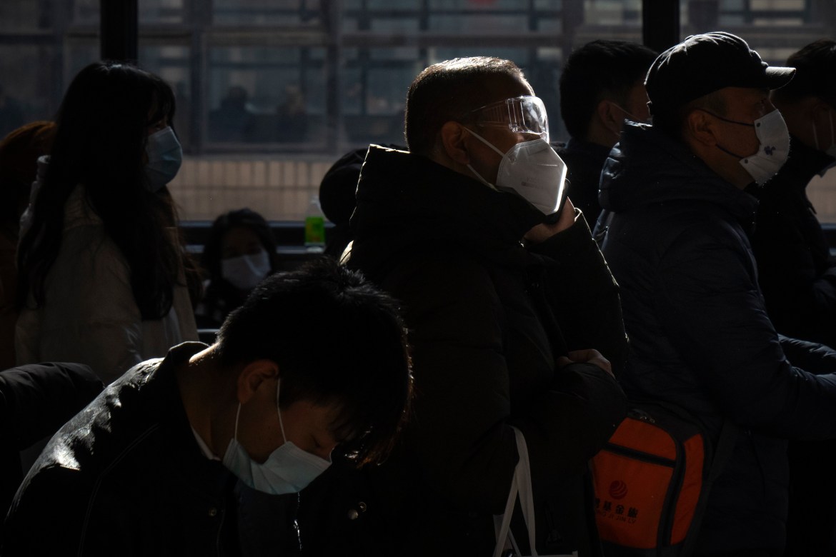 A traveler wearing goggles and a face mask stands in line to board a train at Beijing West Railway Station in Beijing