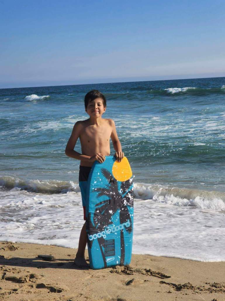 Honor Beauvais, California sahilinde tatilde, mayo giymiş ve boogie tahtası taşıyor.