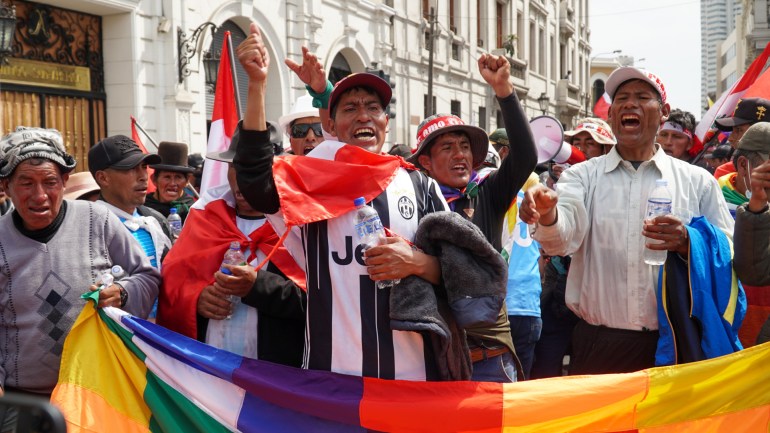 Demonstranten achter een kleurrijk spandoek zingen en steken hun vuisten op in de straten van Lima, Peru.