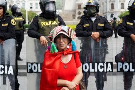 A woman stands before a wall of riot police in central Lima, Peru.