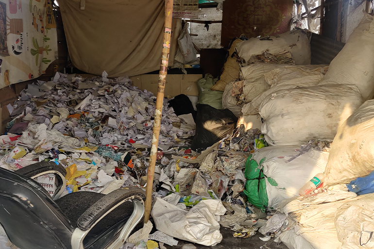 A small warehouse with bags of things on the right side and a pile of papers and other bits of trash on the left.