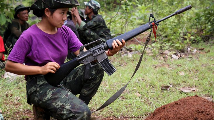 A Karenni woman in a military training session with a weapon. She is wearing a purple t-shirt and fatigues. She looks focused.