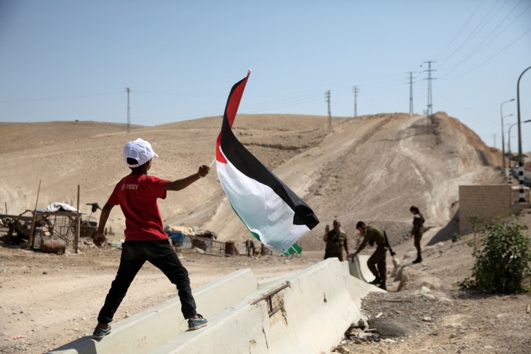 A Palestinian Bedouin boy waves a Palestinian flag in front of Israeli soldiers at al-Khan al-Ahmar near Jericho in the occupied West Bank July 4, 2018