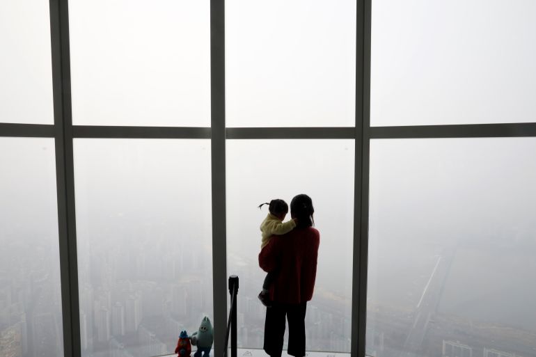 A woman holding her baby in her arms looks at a view of Seoul shrouded by fine dust.