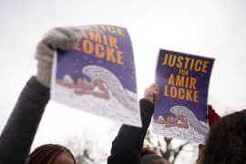 Protesters hold up signs that read "Justice for Amir Locke" with an image of Amir as a sleeping angel