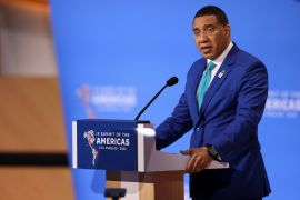 Andrew Holness at a podium, speaking into a microphone against a blue background at the Summit of the Americas