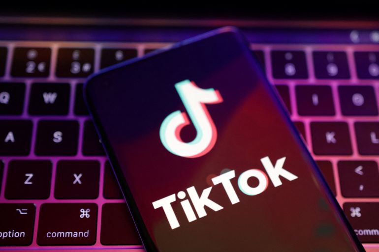 The TikTok app logo appears on a smartphone screen. The phone is laid over a laptop keyboard.