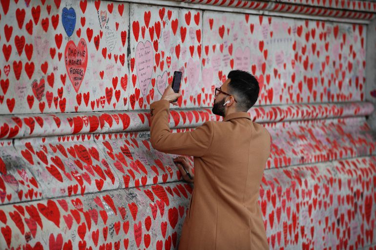 A man takes a photograph of a message on the National Covid Memorial Wall, a dedication of thousands of hand painted hearts and messages commemorating victims of the COVID-19 pandemic, in London, Britain, October 4, 2022. REUTERS/Peter Nicholls