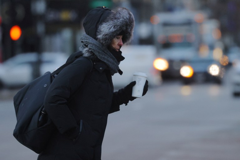 A pedestrian in a furry-lined coat walks through Boston with a coffee cup in hand