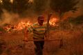 A resident works during a wildfire in Santa Juana, near Concepcion, Chile. Fire and smoke can be seen close behind as he carries what appears to be a spade.