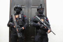 Two police officers on patrol at the court in Jakarta. They are in full riot gear wearing helmets and carrying weapons. Their faces are covered as well.