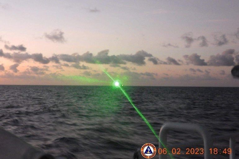 A bright green light coming from the direction of a Chinese Coast Guard ship near Second Thomas Shoal. It is nearly dark. The ship is silhouetted on the horizon.