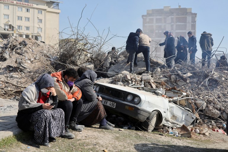 People sit as others search amid the rubble in the aftermath of a deadly earthquake