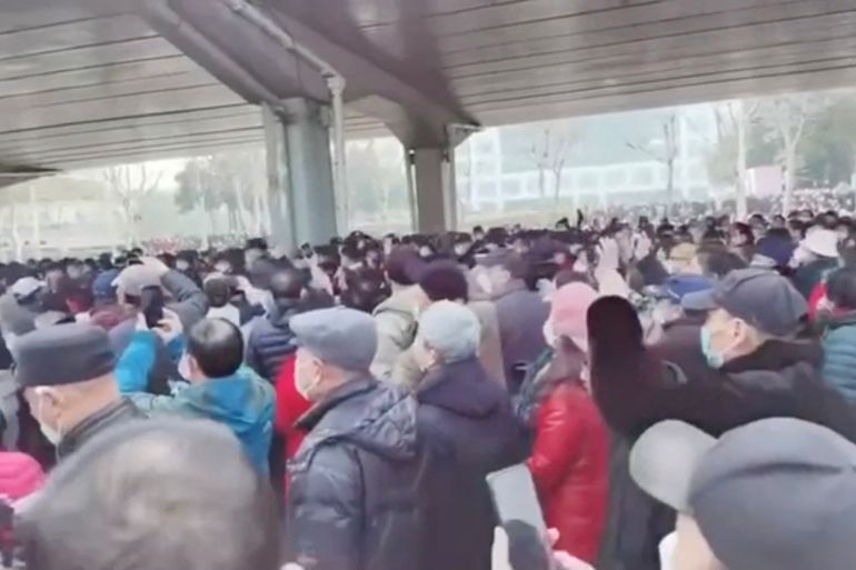 A crowd of people in winter clothing gathering beneath an underpass in Wuhan. Some have grey hair