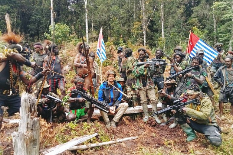 Philip Mehrtens sitting on a log in the forest with the group of TPN-PB fighters who took him hostage in February, Thet have weapons and there are Papuan flags. The pictures was released in March.