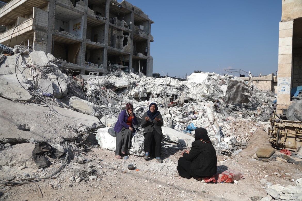 Asmaa' Kousa holds her hands up in prayer as she sits atop the rubble of a destroyed building