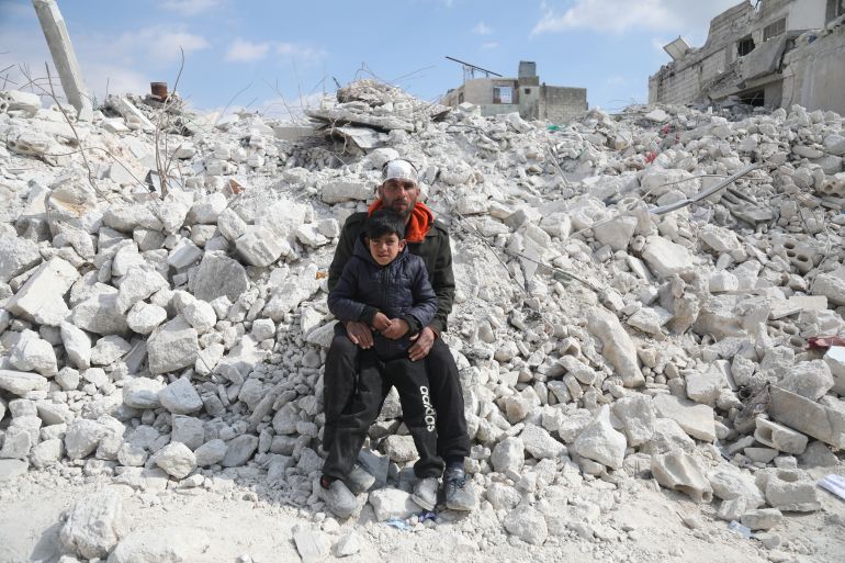 Mahmoud Omar al-Ormi sits with his son Ahmad amid the rubble of their building in Atarib
