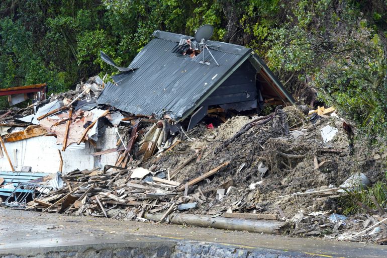A house destroyed in Cyclone Gabrielle. The roof is intact, but the wooden walls have collapsed and there is debris all around.