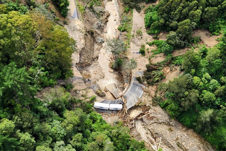 A lorry stranded amid brown mud and debris from landslides near Wairoa in New Zealand. It is an aerial view. There are lots of trees around the road