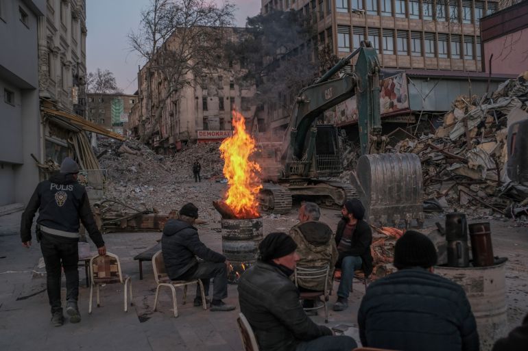 People warm up next to a fire as they take a break from working on removing rubble of collapsed buildings 