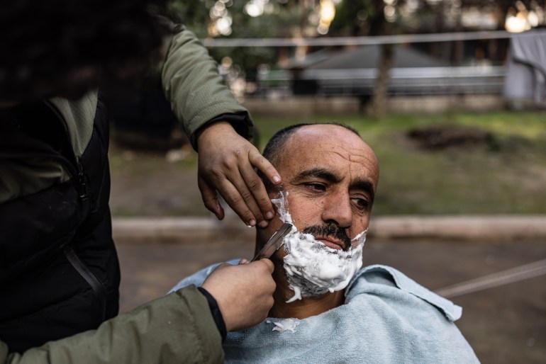 Syrian Khaled al-Hamo is having a hair cut by his 18-year-old son Mohammed al-Hamo, in front of his tent at a makeshift camp in the city of Antakya on February 19, 2023.