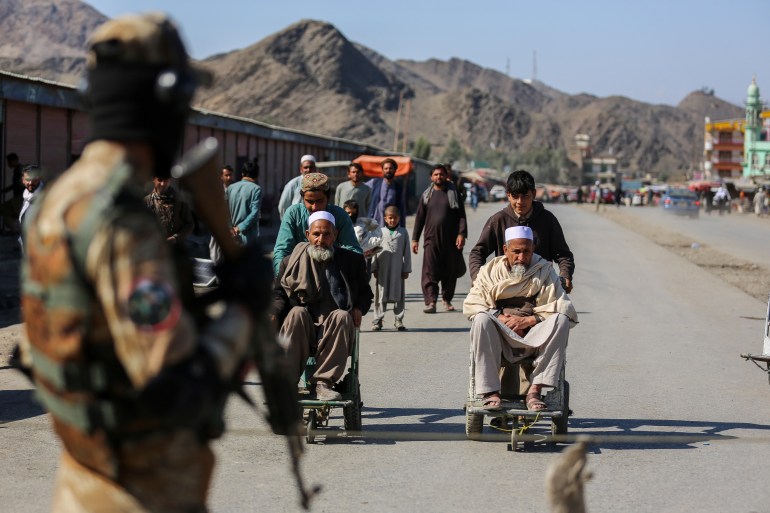 A Taliban security personnel stands guard as young Afghan boys help elderly men in wheelchairs after an incident of gunfire between Afghanistan and Pakistan border forces near the Torkham border 