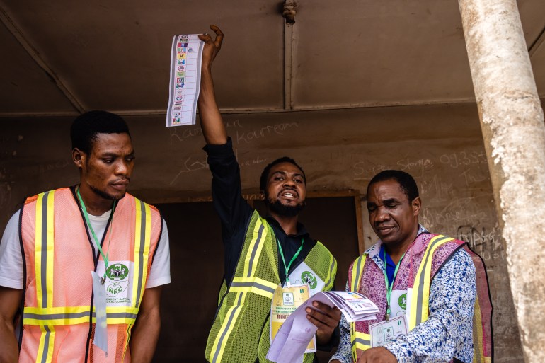 Seorang petugas memegang surat suara dengan dua petugas pemilu lainnya di sisinya.