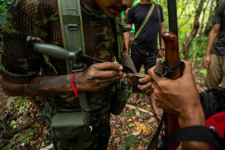 A close-up of a fighter adjusting his weapon with a knife. Another fighter is next to him and also has a gun. The picture does not show their faces. The photo is taken in the jungle.