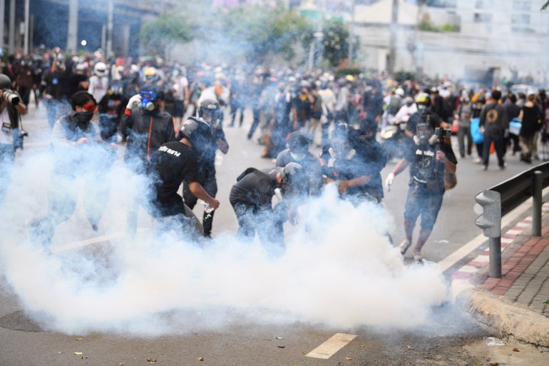 Protesters in Thailand rush to extinguish a tear gas canister fired by police. There is lots of white smoke