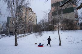 A woman hauls her child through the snow in Kyiv as Russia is believed to be preparing for a new offensive in eastern Ukraine [Evgeniy Maloletka/AP]