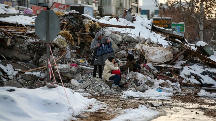 People sit by a collapsed building in Malatya, Turkey.