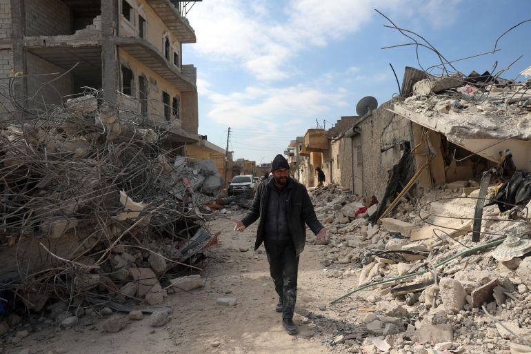 A man walks past collapsed buildings following a devastating earthquake in the town of Jinderis, Aleppo province