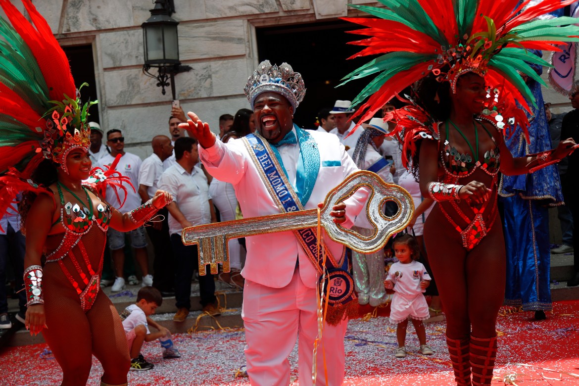 A man in a white suit holds a big, decorative key amid a parade