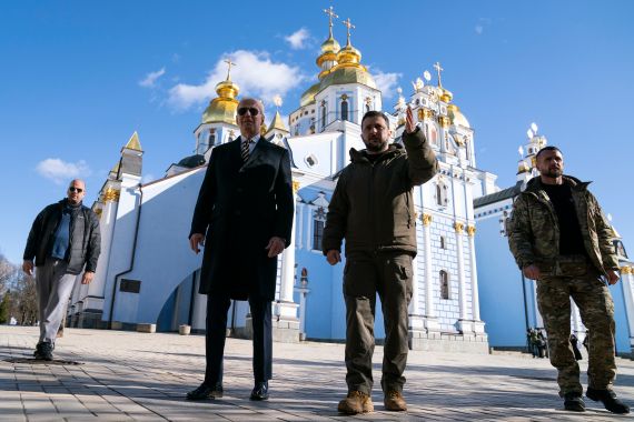 US President Joe Biden, centre left, walks outside with Ukrainian President Volodymyr Zelenskyy with Kyiv's Saint Michael's golden-domed Cathedral behind them. They are accompanied by two men.