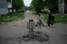 People walk past part of a rocket that sits wedged in the ground in Lysychansk