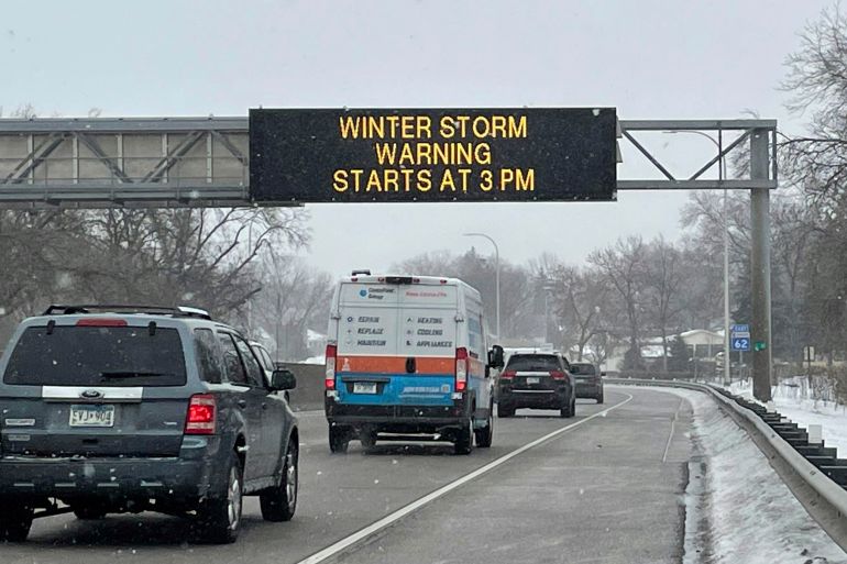 A traffic sign over a highway reads: “Winter storm warning: Starts at 3 p.m.”