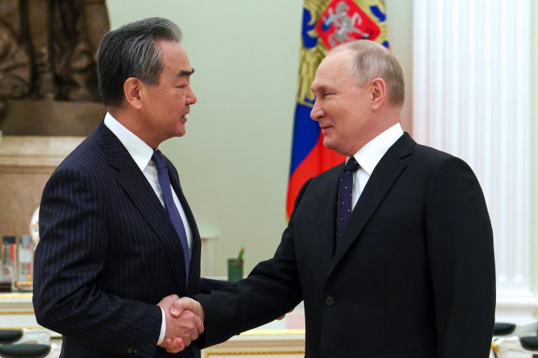 Wang Yi (left) and Vladimiri Putin (right) shake hands as they meet in the Kremlin. There is a flag behind Putin