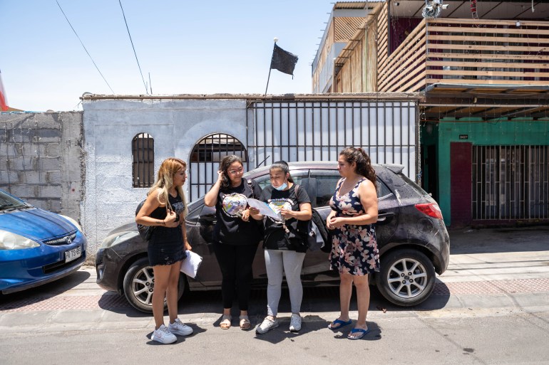 Four women huddle around a document in front of a car in the neighbourhood of Cerro Chuño