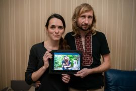 A photo of Oksana Slipchenko and her husband Sergio Skudin, with Oksana showing their wedding day photo with both of them dressed in vyshyvankas.