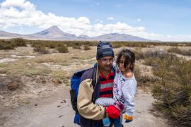 A man carries a little girl in his arms across the Altiplano highlands.