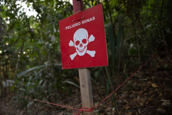 A read sign that reads, in Spanish, "Danger: Mines" sits outside a forested area