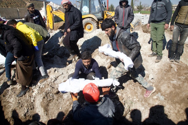 Men hand over the wrapped bodies of babies or small children for burial in a mass grave