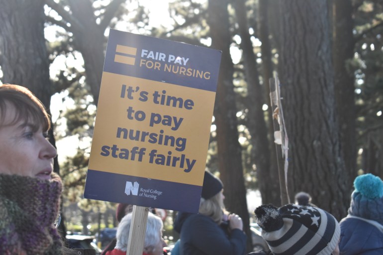 A photo of someone holding a sign with the words "Fair pay for nursing" on top and "it's time to pay nursing staff fairly" on the bottom half with a logo of the Royal College of Nursing at the bottom of the sign.